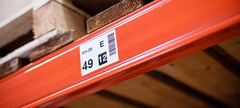Etykieta z kodem kreskowym i numerem naklejona na pomarańczowy regał w magazynie