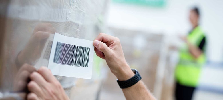 Etykieta z kodem kreskowym przyklejana na pudełko z folią termokurczliwą w magazynie